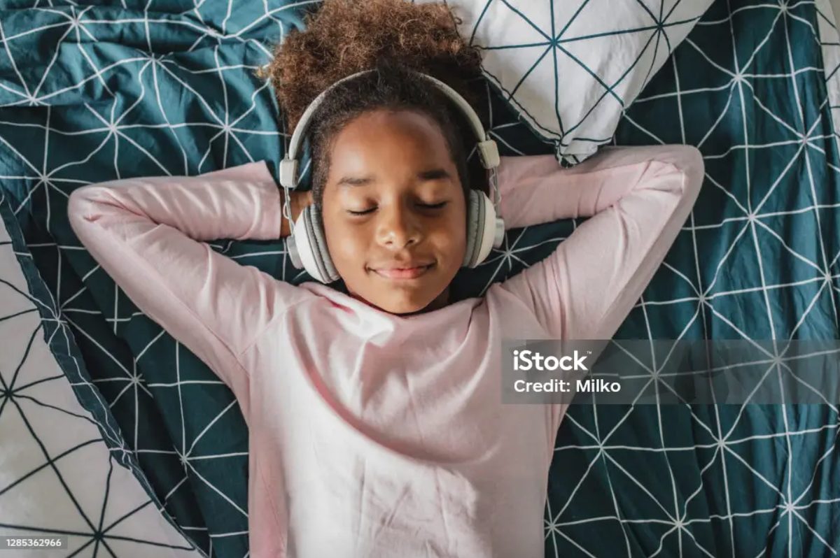 A girl lying down with headphones on, eyes closed and content, listening to music
